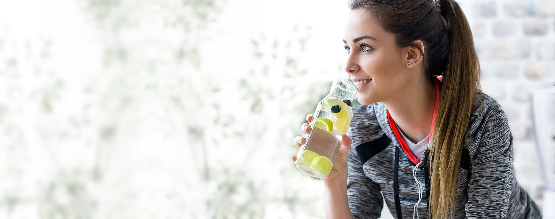 Woman in activewear drinking fruit-infused water from a glass bottle